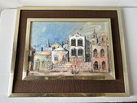 Framed mixed media townscape painting showing the front detail with dark brown textured mat and silver frame.