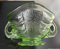 Close-up of green glass bowl showing one elephant handle and textured panel.