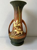 Front view of Roseville Zephyr Lily Vase showing raised lily flowers on brown and green glaze with two handles.