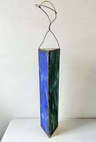 Vertical image of the triangular prism-shaped stained glass kaleidoscope showing one blue panel and one green panel with wire hanger attached on top.