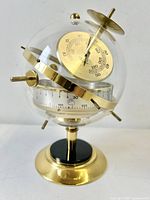 Front view of glass globe with brass thermometer and barometer visible, mounted on brass and black base.