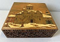 Box front view showing carved floral sides and top lid with detailed pyrography and enamel artwork of Russian Orthodox church in winter.