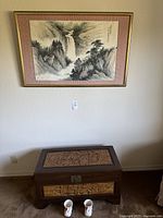 Overall photo showing framed painting of waterfall landscape above carved wooden trunk with latch and Asian motifs.