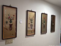 Four vertically framed Asian art floral panels hung on wall, showing full lot contents.