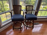 Pair of wooden bar stools with cane backs and blue upholstered seats shown against a large window