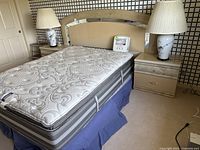 Full view of queen mattress on box spring with bed frame, headboard, nightstands and lamps