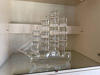 Clear crystal ship sculpture shown front-right angle on a shelf, highlighting the hull and sails