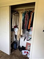Full view of closet showing hanging garments, boots on floor, shopping bag and artwork