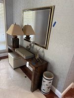 Full view of entry table with mirror, lamps, deer sculptures, patterned box, ottoman, and ceramic stand