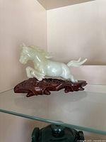Front angled view of jade horse sculpture on wooden base showing detailed carving and light green hue.