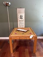 Full front view of Mahjong table with tiles, scroll, and floor lamp in background.