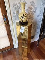 Yellow ceramic vase with hand-painted birds and floral design on carved wooden stand in front of wallpaper.