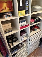 White cubby shelving showing shoeboxes, folded tops, belts and a spray can