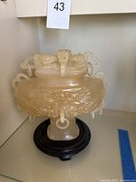 Front view of the pale yellow jade vessel with lid on wooden stand