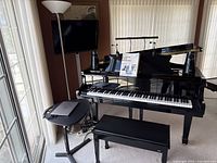 Front view of grand piano and bench with sheet music, wall-mounted TV, floor lamp and side table with laptop (non-included).