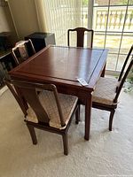 Angled front view of square rosewood finish game table surrounded by four matching wooden chairs with beige fabric seats