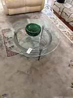Round glass coffee table with metal frame and green blown glass bowl on top, showing full view of table and decor.