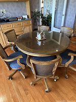 Overall view showing round wooden table with glass top and six blue cushioned swivel chairs around it on hardwood floor in kitchen setting.