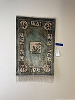 Full view of rectangular wool rug hanging on wall, showing entire design and fringe.