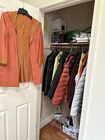 Orange hooded coat hanging on door alongside view into closet with hanging items