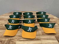 Overview of 12 Oakland A's visors arranged on wooden surface showing front and color.