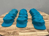 Front view of three rows of teal baseball caps aligned on wooden surface, showing flat brims and button tops