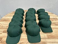 Sixteen hunter green baseball caps arranged in four rows on a wooden surface.