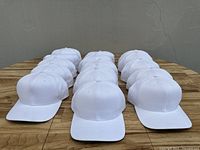 Front view of 16 white baseball caps arranged in 4 rows on a wooden surface.