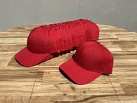 Photo showing all 16 red baseball caps stacked horizontally on a wooden surface, with one cap displayed in front to show details.