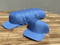 16 baby blue baseball caps arranged in a line on a wooden surface under bright lighting showing their structured shape and curved brims