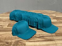 Photo showing 16 teal green baseball caps in a row, illustrating the color, shape, and overall condition.