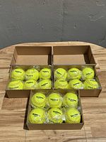 Three cardboard boxes each containing six yellow Richardson softballs, individually wrapped in plastic.