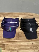 Two stacks of visors on wooden surface: left stack of purple Arizona Diamondbacks visors and right stack of black Chicago White Sox visors