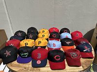 Front view of all 20 caps arranged in four rows on a wooden surface, showing various team logos and colors.