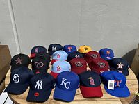Photo showing all 20 baseball caps arranged on a wooden surface with clear view of team logos and colors.