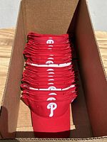 Photo of a cardboard box filled with 20 red Philadelphia Phillies visors stacked vertically showing the front logos.