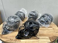 Group of 5 Cooper 1000 black catcher's helmets on wooden table, four wrapped in plastic and one unwrapped.