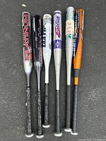 Six aluminum baseball bats arranged horizontally on dark surface, showing varied brands and colors.