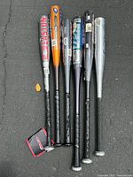 Photo showing all six bats laid out side by side on pavement, displaying varied colors and grip styles.
