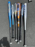 Overview of six aluminum baseball bats in various colors and brands, standing upright on black ground.