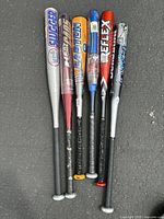 Full group of 6 aluminum baseball bats standing upright showing various brand names and colors.
