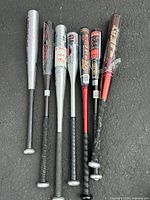 Photo of six aluminum baseball bats on pavement, showing varied brands and colors