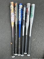 Photo showing all six aluminum baseball bats grouped side by side, grips facing down and barrels up. Various brands and colors visible.