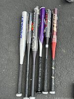 Six aluminum baseball bats laid on the ground showing entire bats with handles and barrels.