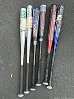 Photo of all six aluminum baseball bats laid side by side on pavement, showing different colors and brands