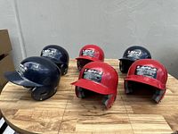 Group of six Rawlings batting helmets placed on a wooden surface, three navy blue and three red.