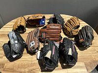 Overview of 8 baseball gloves laid out on table showing various brands and colors.