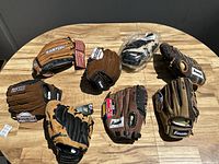Eight baseball gloves arranged on a wooden table showing variety of brands and conditions.