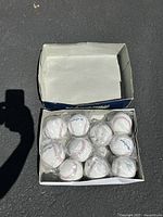 Photo showing approximately 12 MacGregor branded baseballs, individually wrapped in plastic and neatly arranged inside their original cardboard box.