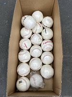 Box containing approximately 16 white baseballs with red stitching, mostly Dudley branded, some labeled Lightning. Includes two sealed baseballs and one with a barcode sticker.